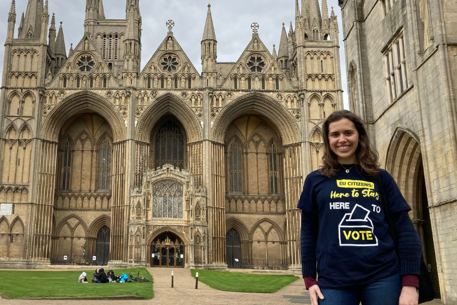 Young woman smiling in front of Houses of Parliament, wearing #OurHomeOurVote T-shirt